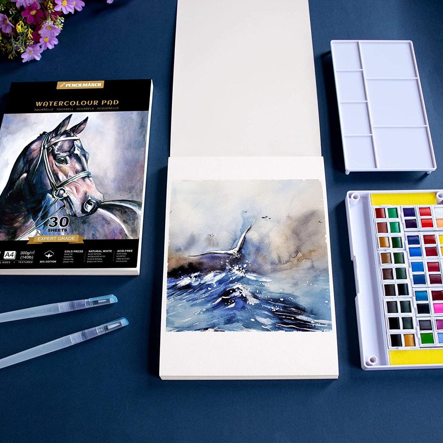 An A4 Pencilmarch artist watercolour paper pad with 300 gsm paper and 30 pages next to a painting of the sea and a paint palette - Stationery Island